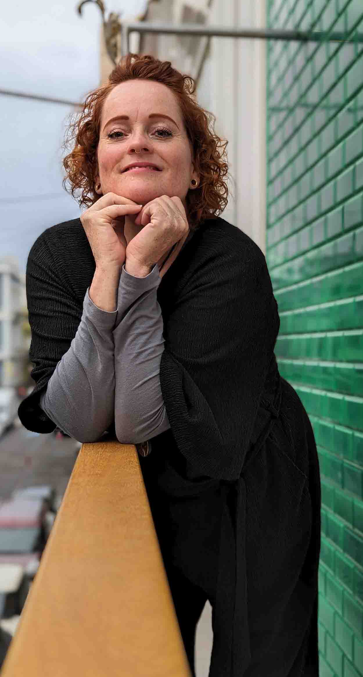 ginny-warner-doula-bij-rouw-en-sterven-open-portret Ginny Warner leunt ontspannen op een reling, met een open blik als doula bij rouw en sterven